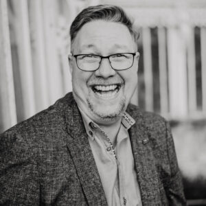 Black and white photo of JD Gibson voiceover laughing and looking at the camera.
